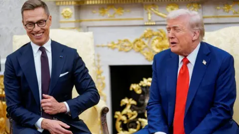 Reuters A smiling Alexander Stubb is adjusting the button on his blue suit sat in Oval Office alongside a laughing Donald Trump who is wearing a blue suit and red tie. 
