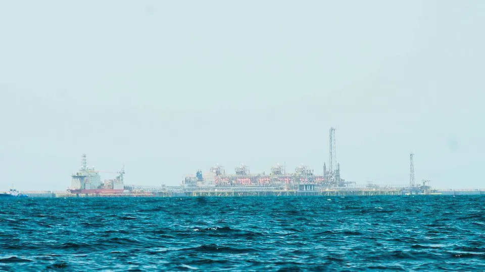 A gas platform out at sea can be seen on the horizon - the ocean can be seen in front of it and above a large view of the sky.