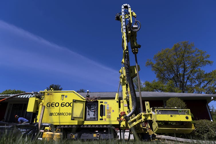 A large yellow vehicle with a tall tower on it stands in front of a house.