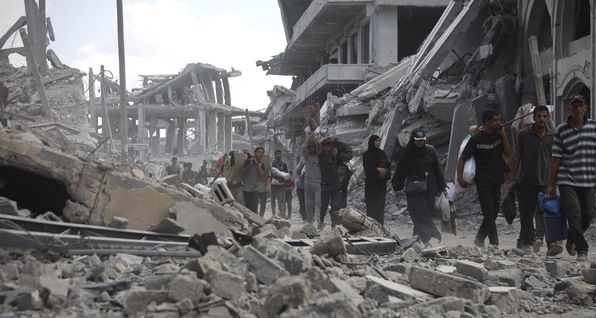 Mehrere Menschen laufen durch eine Straße voller Schutt und eingestürzter Gebäude. Im Hintergrund sind schwer beschädigte Betonbauten zu sehen.