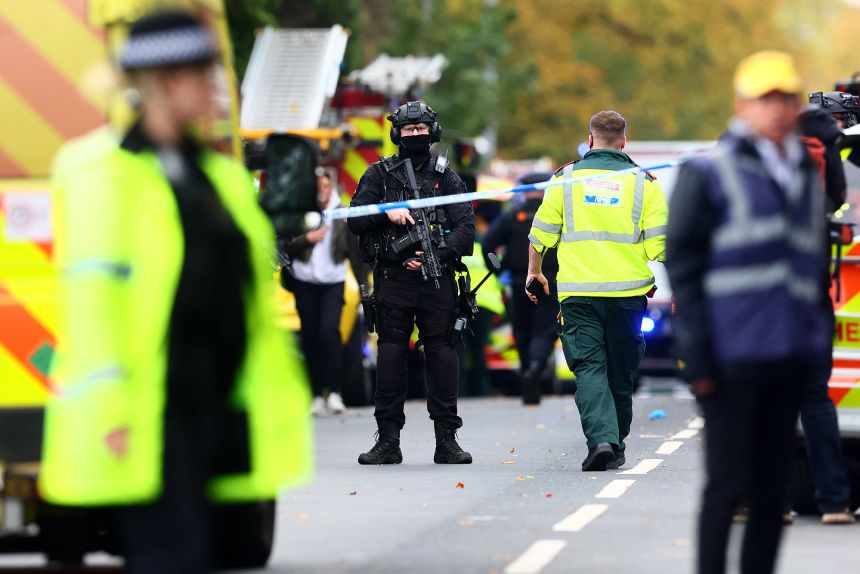 Armed police officers stand with their weapons inside a police cordon near Heaton Park Hebrew Congregation synagogue in Crumpsall, north Manchester, on October 2, 2025, following a stabbing and vehicle attack.