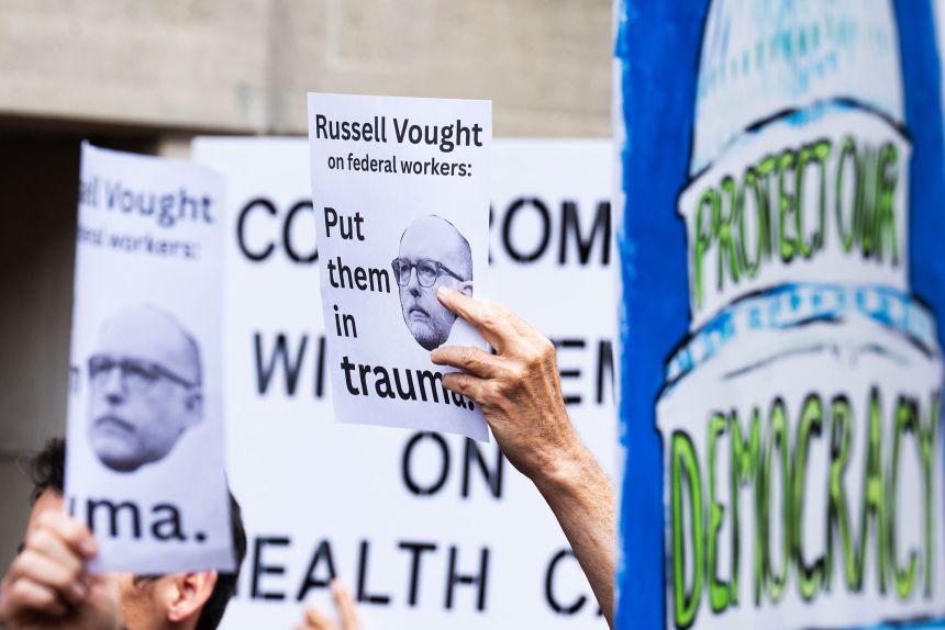 Signs showing OMB Director Russell Vought during a news conference with Maryland and Virginia congressional Democrats in Washington, DC, on October 14, 2025.