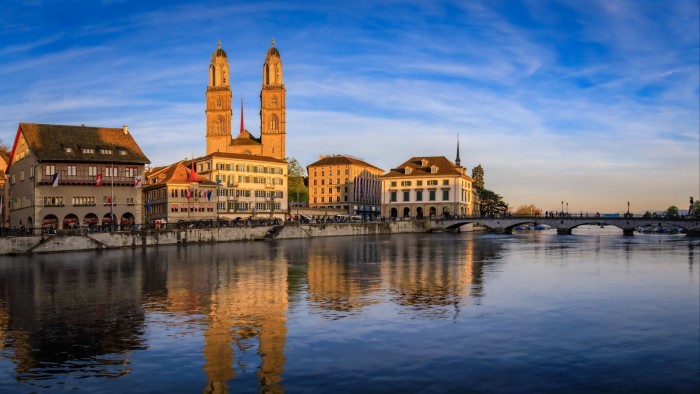 Zurich cityscape featuring the twin towers of Grossmunster cathedral and the Limmat River at sunset