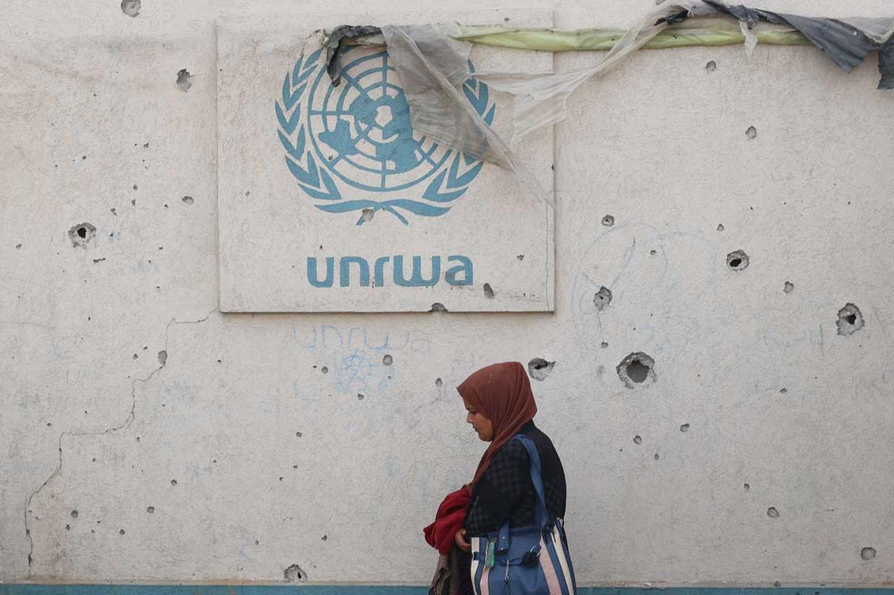 A Palestinian woman walks past a damaged wall bearing the UNRWA logo at a camp for internally displaced people in Rafah in the southern Gaza Strip on May 28, 2024. (AFP Photo)