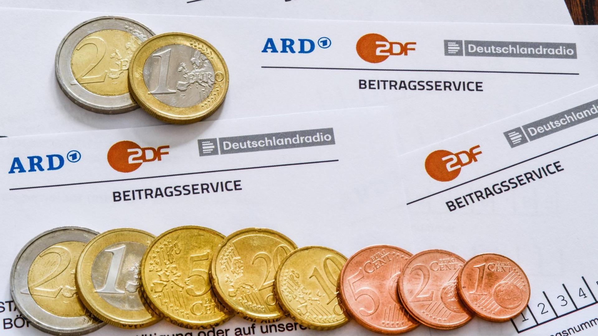 Auf mehreren Formularen des Beitragsservice für den Rundfunkbeitrag liegen Geldmünzen. Auf mehreren Formularen des Beitragsservice für den Rundfunkbeitrag liegen Geldmünzen.