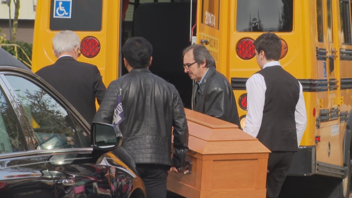 Foue people carry a small casket into the back of a yellow school bus