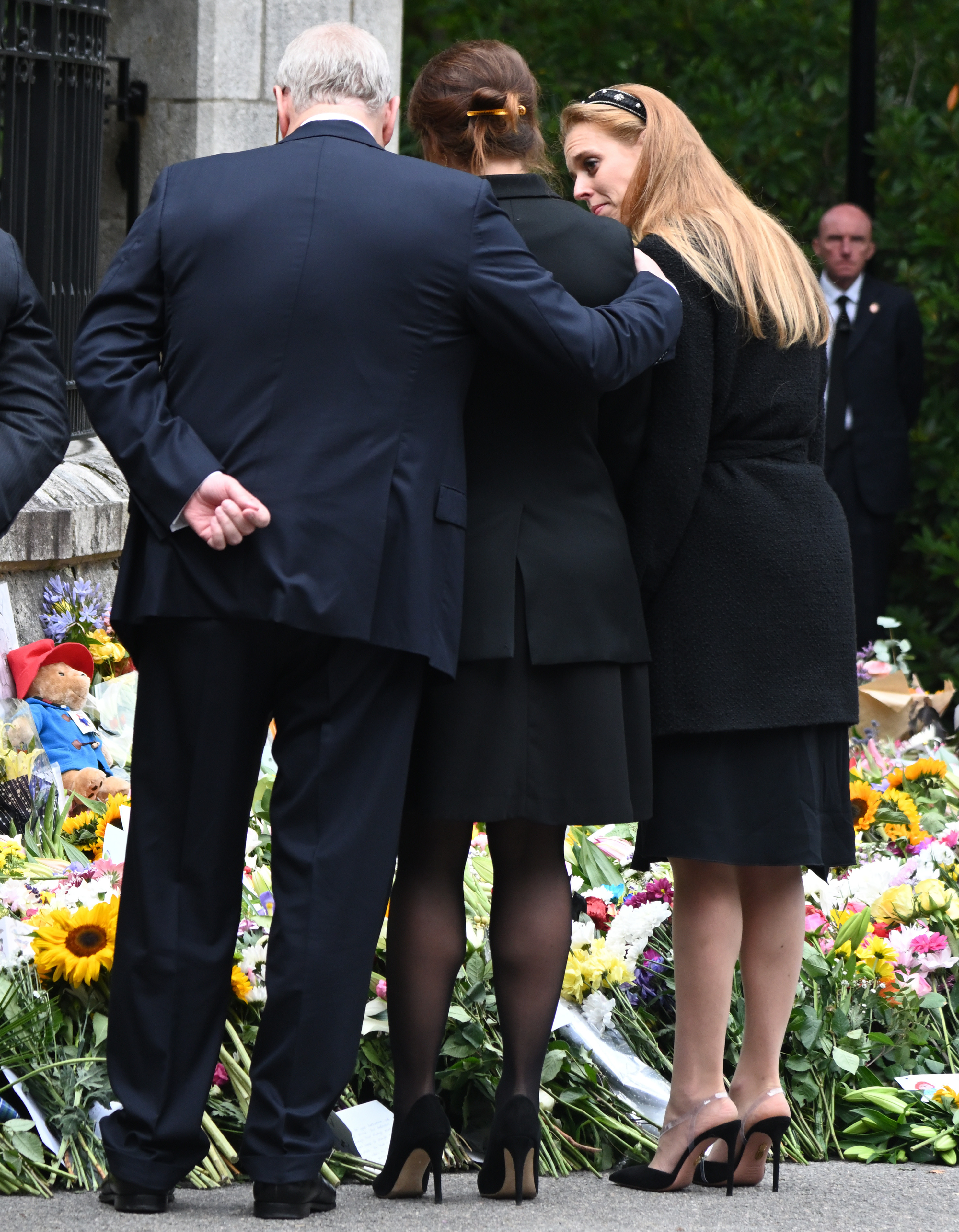 Prince Andrew, Princess Beatrice and Princess Eugenie hugging outside a memorial of flowers for Queen Elizabeth
