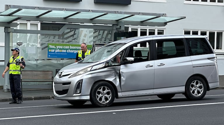 Police officers inspect damage to a car following a crash with an e-scooter rider in Auckland central.