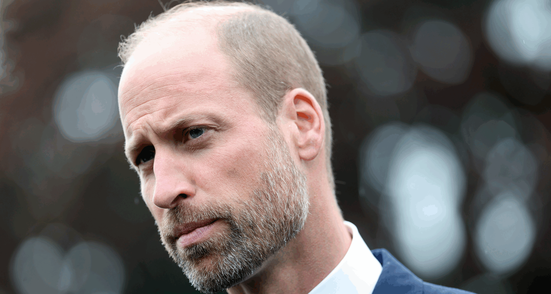 Prince William wearing a white shirt and blue jacket looking stern
