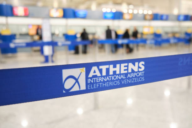 Blue security barrier at Athens International Airport with blurred check-in counters in the background.