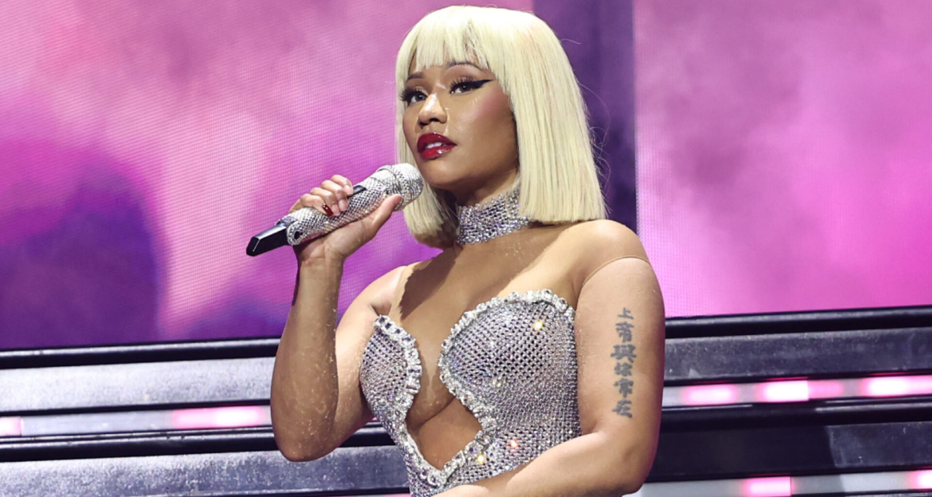 Nicki Minaj performing on stage in a sparkling silver outfit, holding a microphone.