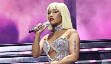 Nicki Minaj performing on stage in a sparkling silver outfit, holding a microphone.