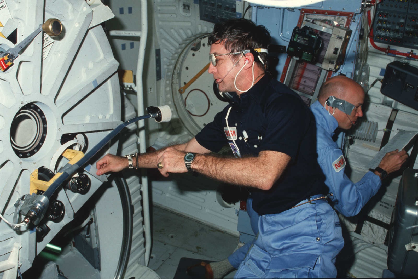 Donald H. Peterson wearing one Rotocall on each wrist during STS-6. Story Musgrave wears another in the background. Image - NASA