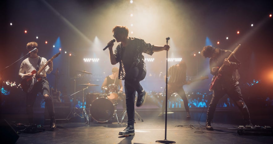 A rock band performing on stage with dramatic lighting as the lead singer sings into the microphone and guitarists play energetically.