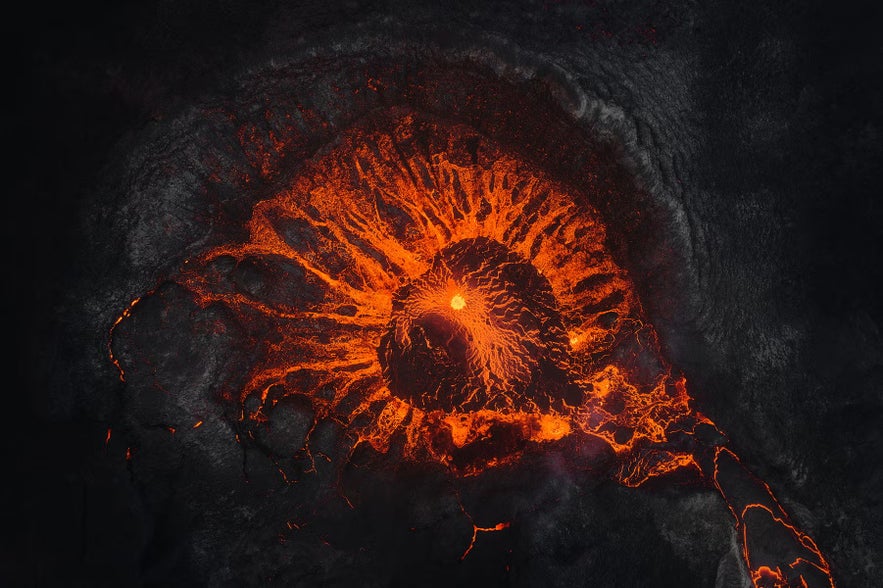 Aerial view of a volcanic eruption with glowing orange lava flowing across dark volcanic rock.