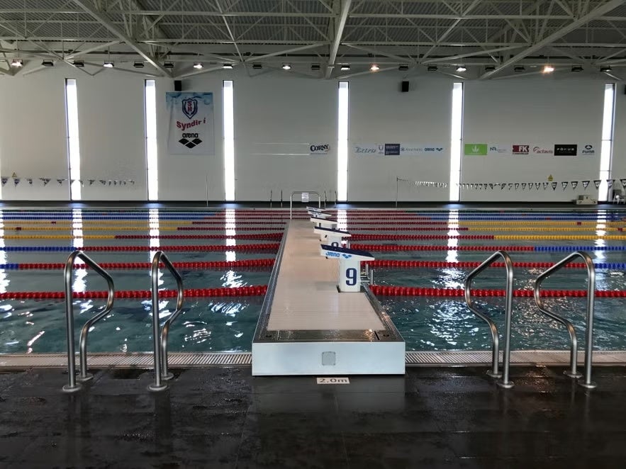 Indoor swimming pool with lane dividers and starting blocks under bright natural light from tall windows.