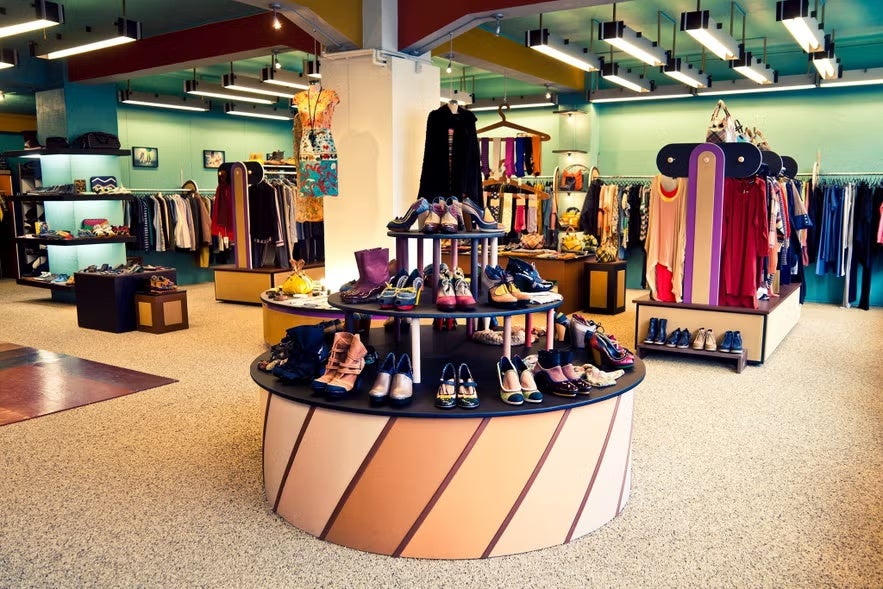 Colorful boutique displaying shoes, dresses, and accessories on racks and shelves in a stylish interior.