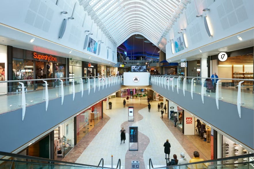 Interior of Smaralind shopping mall in Reykjavik with shops, escalators, and people walking under a glass roof.