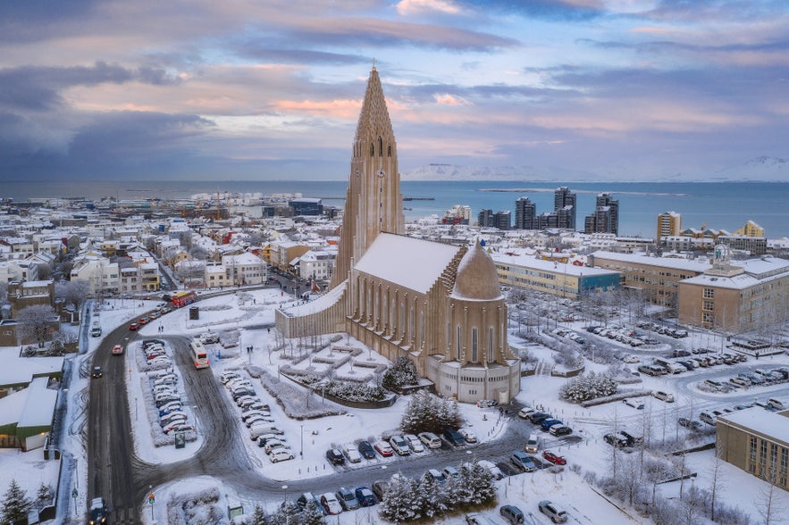 Aerial view of Hallgrimskirkja church and downtown Reykjavik covered in snow with mountains and the ocean in the background.