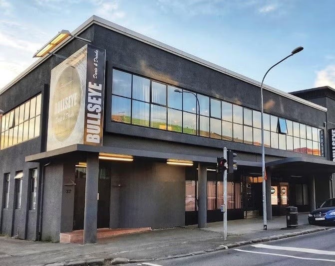 Exterior of Bullseye Dart Club in Reykjavik, a modern gray building with large windows and a street view in front.