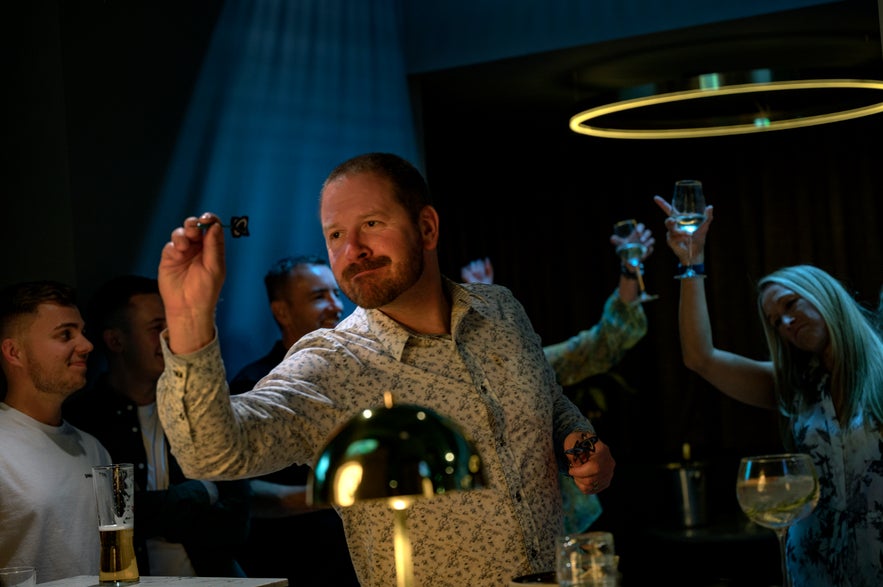 A man throwing darts in a lively bar while friends cheer and raise their glasses in the background.