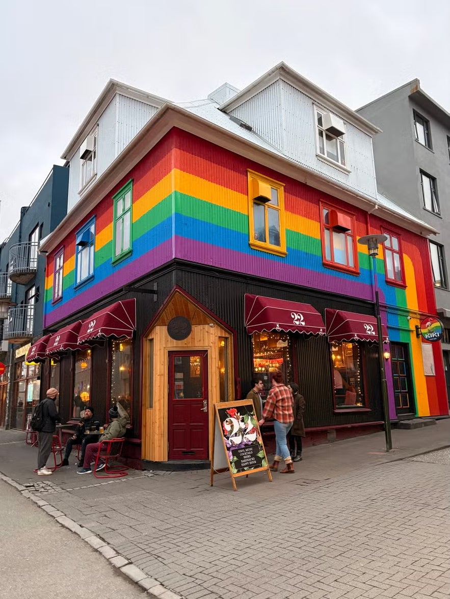 A colorful building in Reykjavik painted with rainbow stripes, housing a café and bar with outdoor seating.