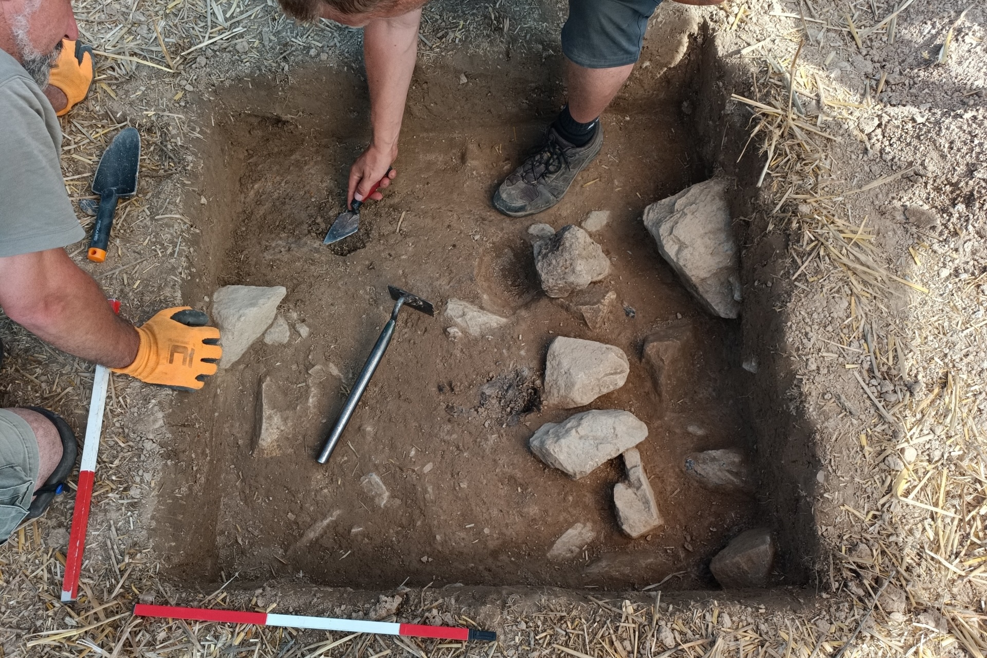 a top view of a rectangular excavated hole with two archaeologists working