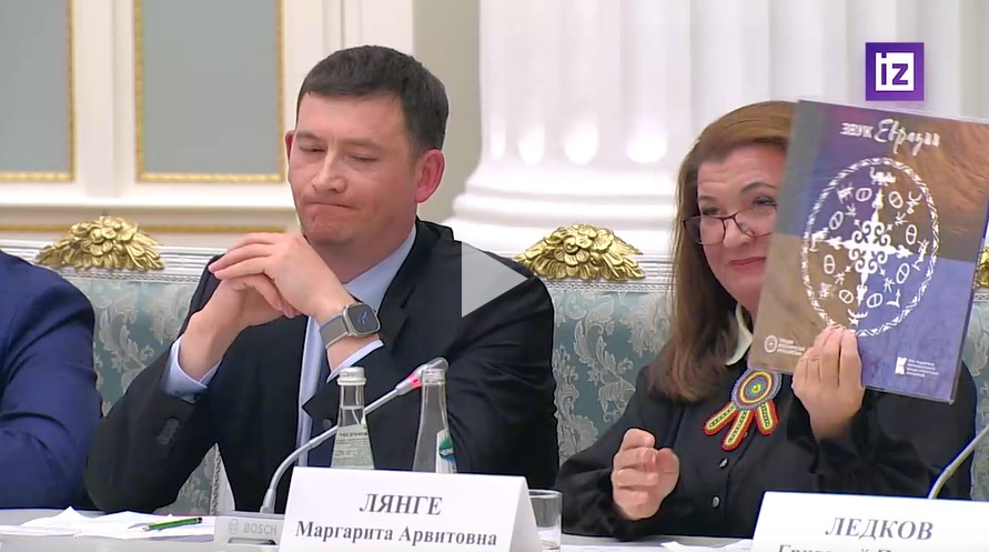 A woman holding up a vinyl record featuring Kalmyk electropunk to Vladimir Putin, who is sitting next to her.