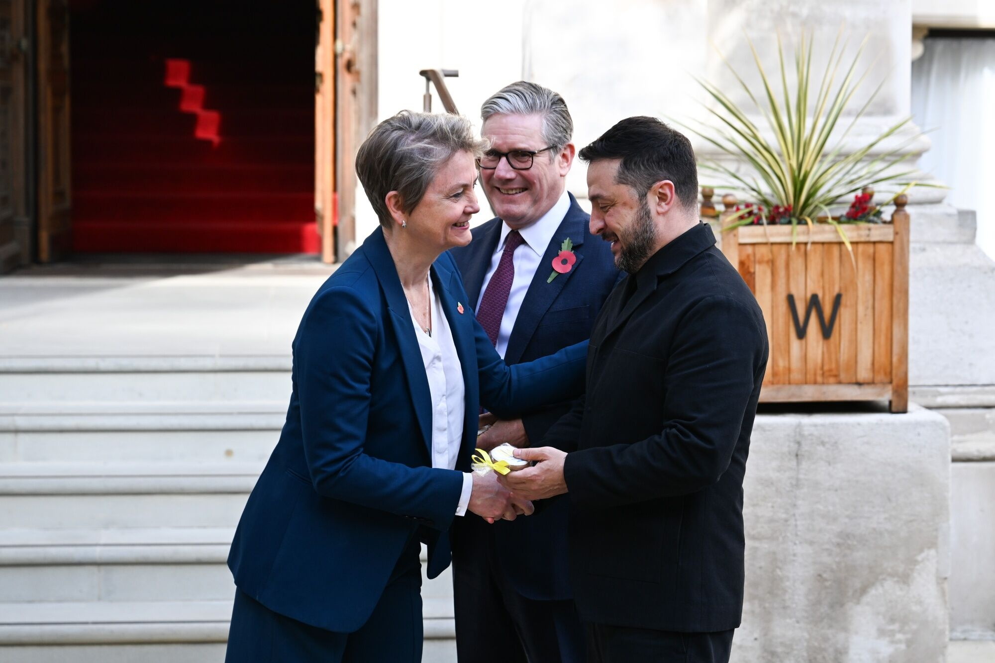 British Foreign Secretary Yvette Cooper shakes hands with Ukraine's President Volodymyr Zelensky, while British Prime Minister Keir Starmer stands between them, smiling.