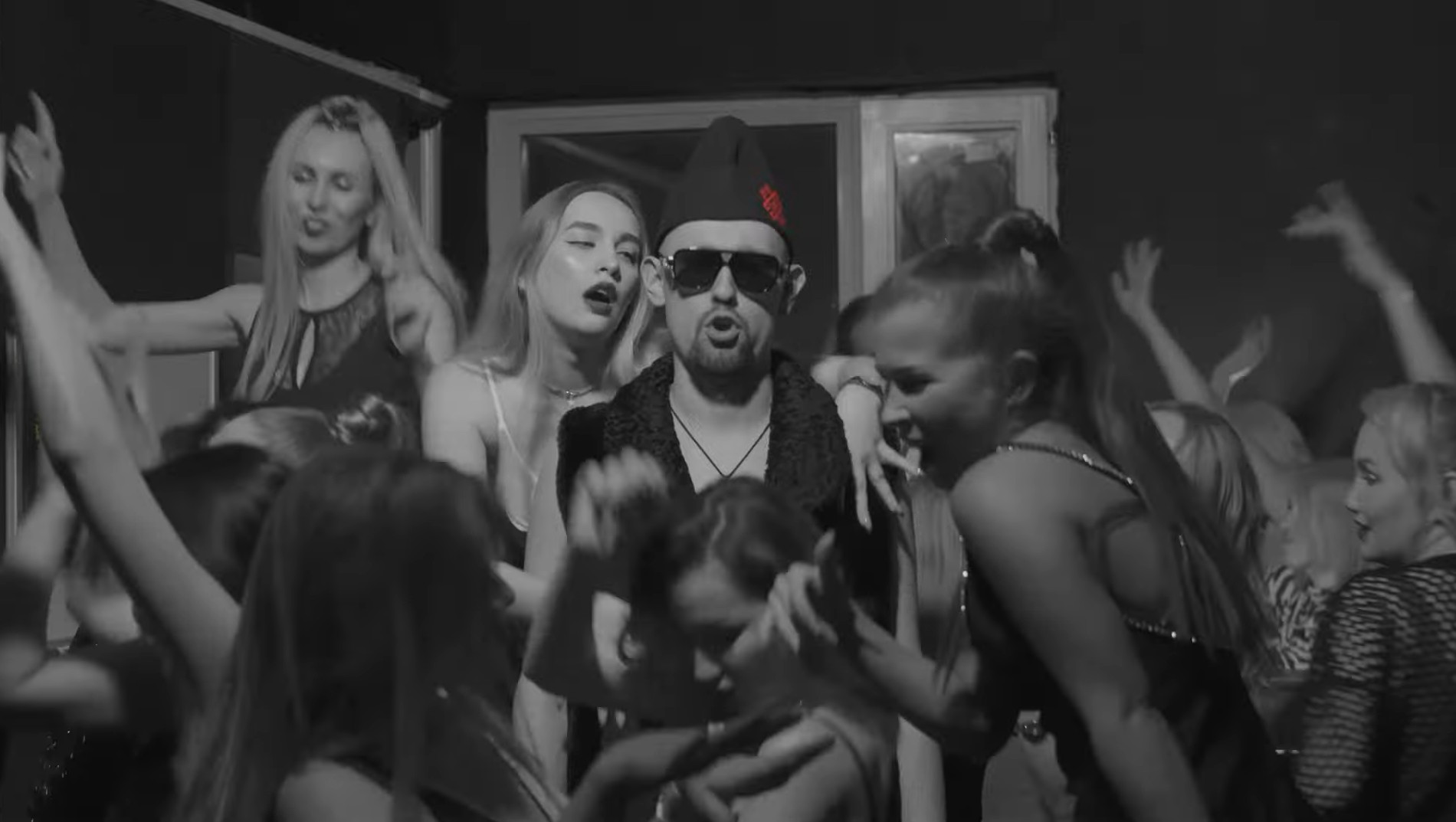 Shyp Lii in sunglasses and a hat surrounded by women dancing at a party.