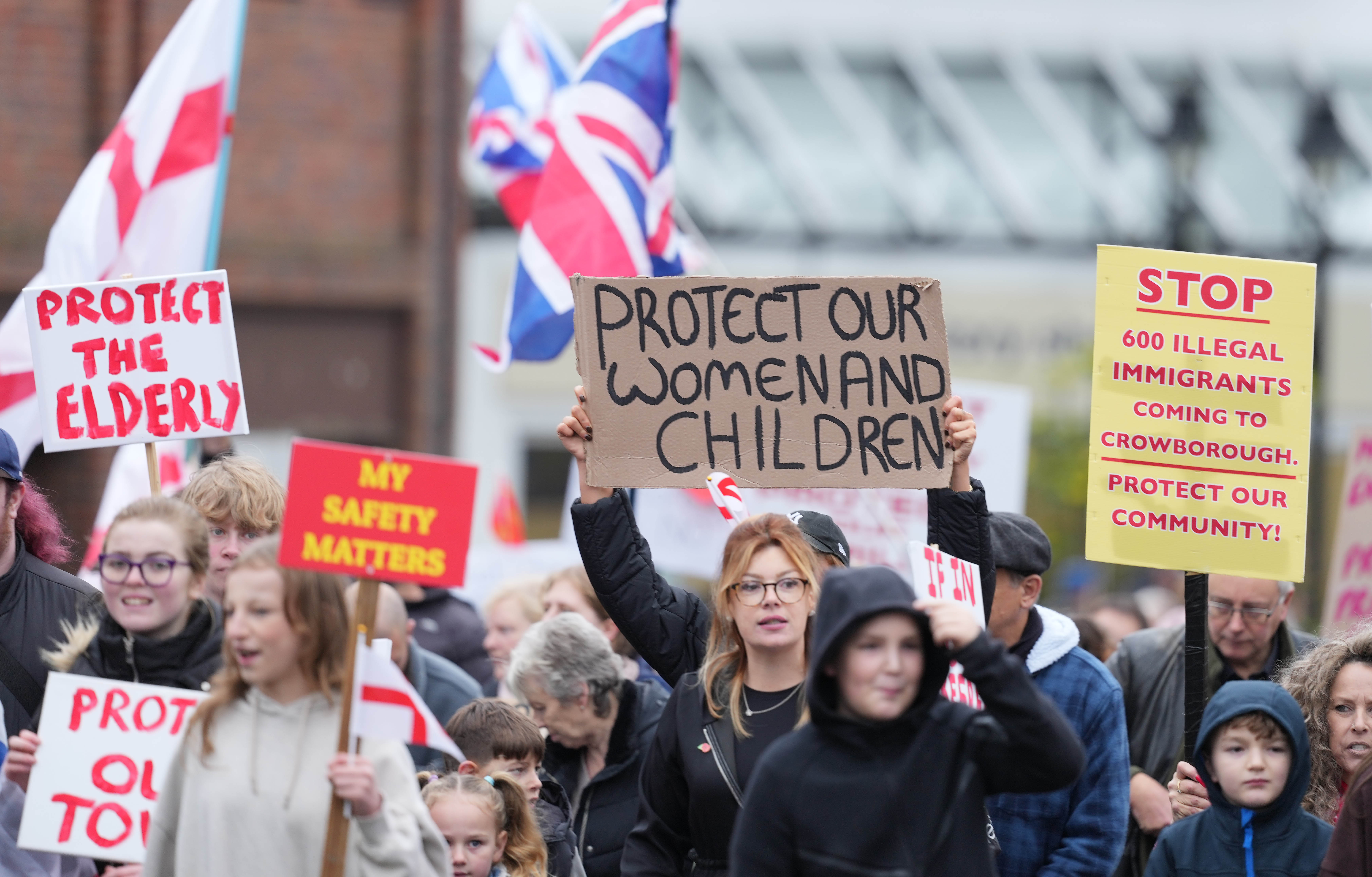 People holding protest signs against migrant camps, with signs saying "Protect Our Women and Children", "Protect the Elderly", "My Safety Matters", and "Stop 600 Illegal Immigrants Coming to Crowborough. Protect Our Community!".