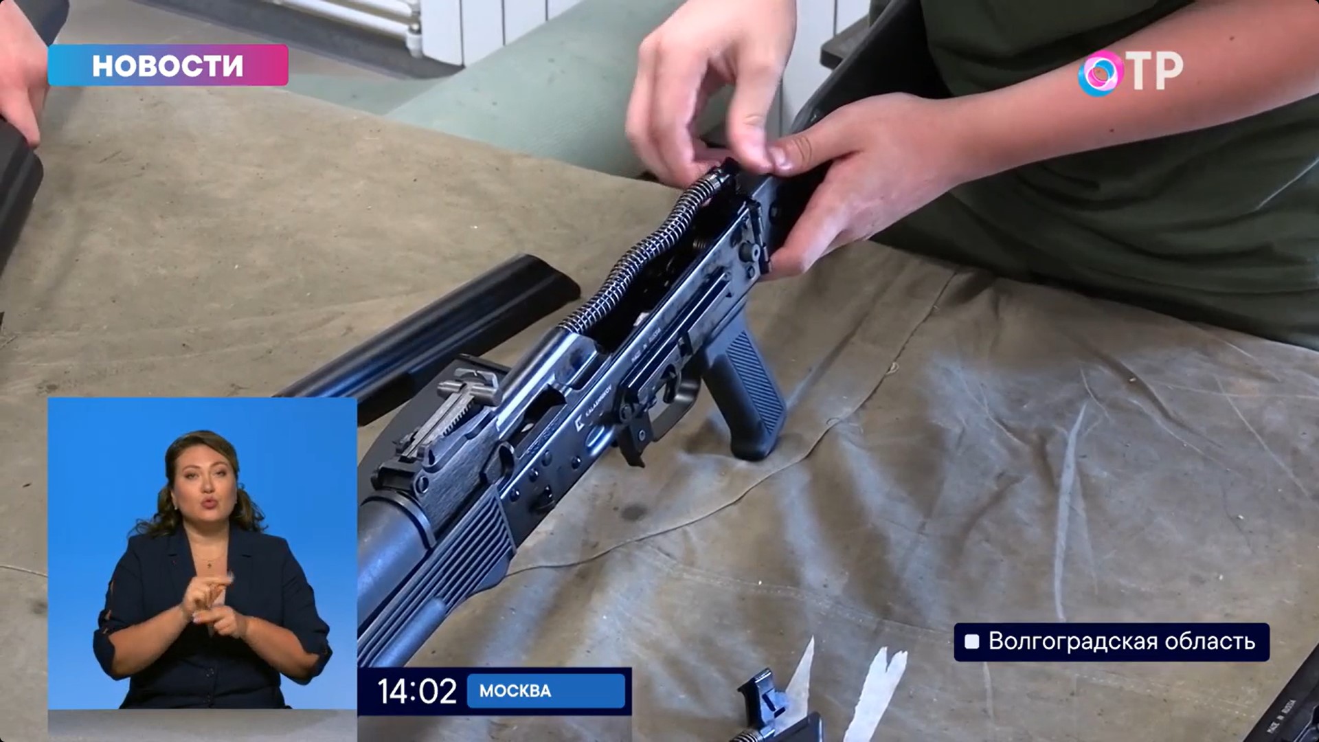 A young person assembling a Kalashnikov assault rifle in a military-patriotic camp in Russia, with a news reporter in a smaller inset.