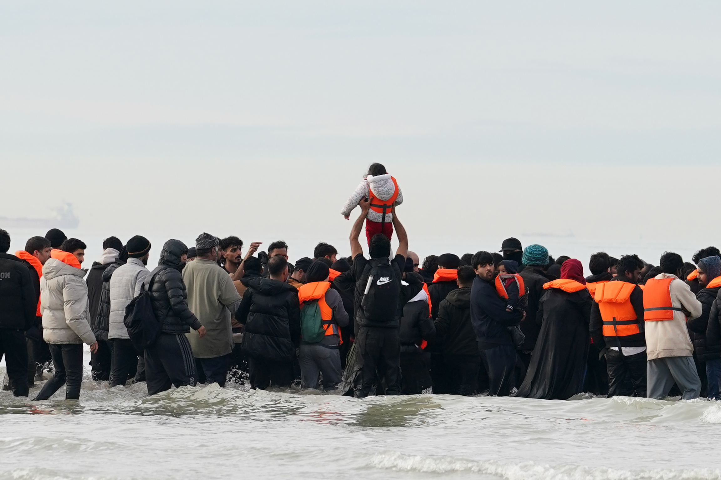People believed to be migrants, including children, in the water and boarding a small boat in Gravelines, France.