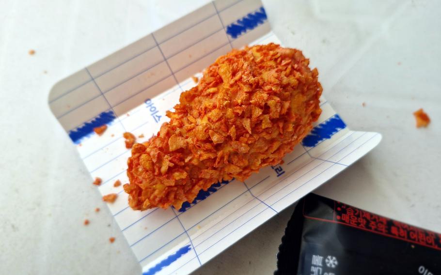 What appears to be a breaded chicken drumstick sits on a cardboard tray.