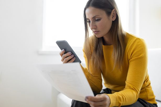 Woman looking at phone and bills