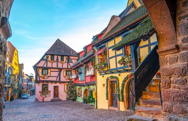 Traditional wreaths hang from windows in a quiet cobbled street in Strasbourg