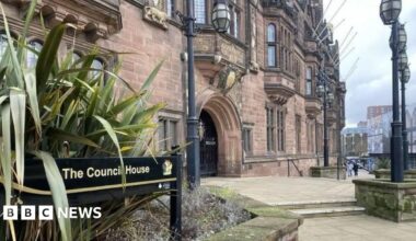 The council offices in Coventry are in a Tudor Revival-style building, built between 1913 and 1917, with an ornate exterior. A sign points to The Council House. People are walking around the building.