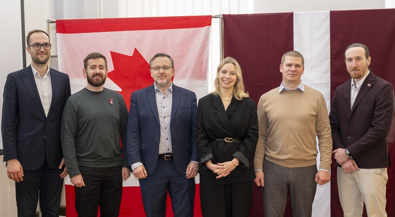 Photo de groupe montrant des représentants canadiens et lettons devant les drapeaux du Canada et de la Lettonie, dont l’ambassadeur du Canada et une responsable du ministère de la Défense, entourés de membres de la « CyTF 2 » et du « CERT.LV ».