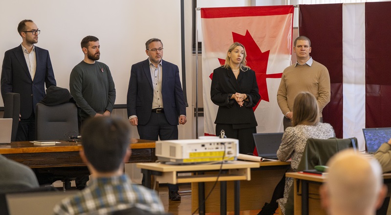 Des représentants canadiens et lettons s’adressent aux participants devant les drapeaux du Canada et de la Lettonie à l’ouverture du « Threat Hunting Workshop ».