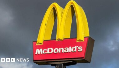 A large McDonald's sign with the yellow arches stands in front of a gloomy grey sky.