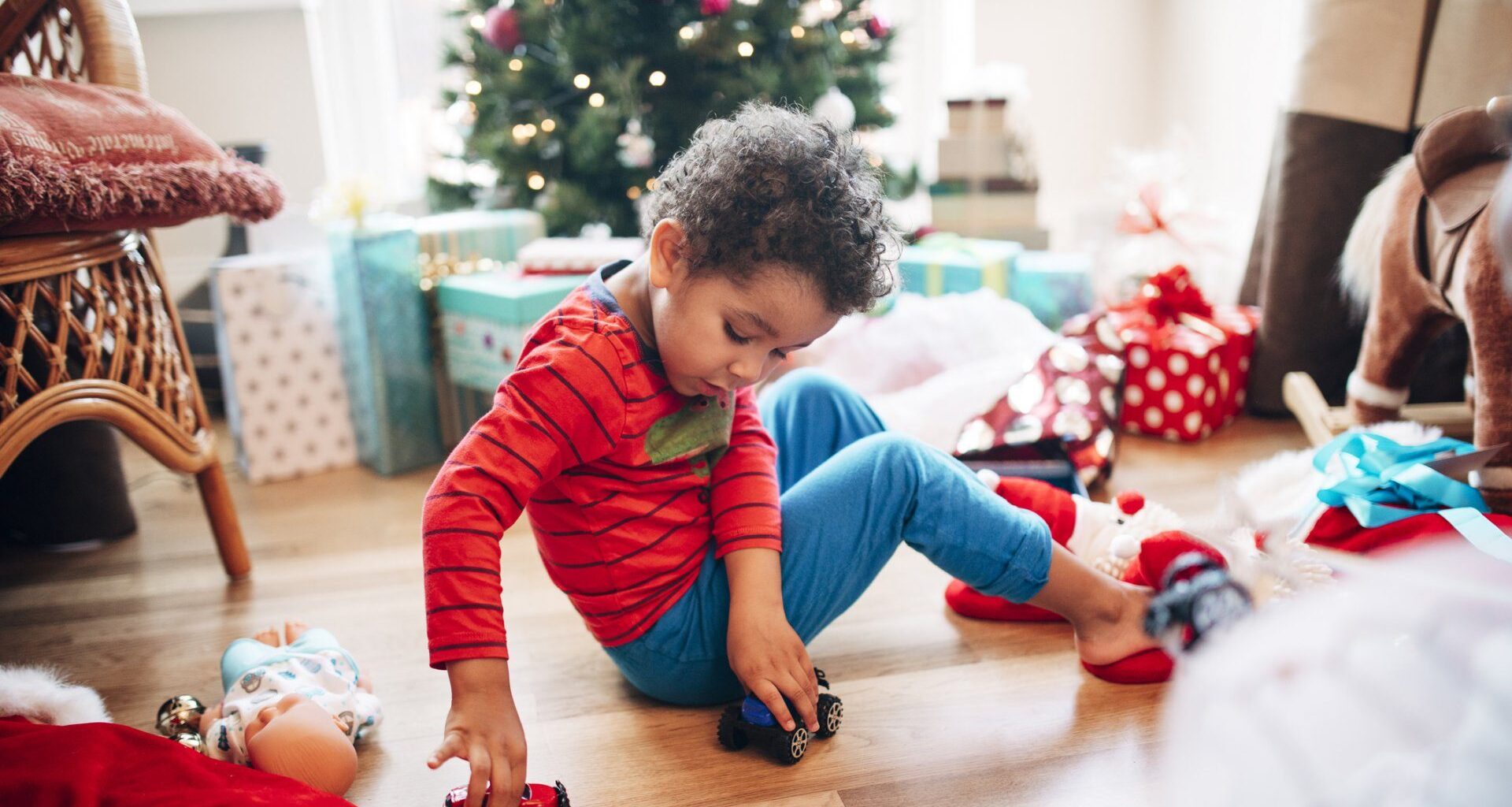 A little boy plays with some toy cars he has received as a Christmas present in front of the Christmas tree.