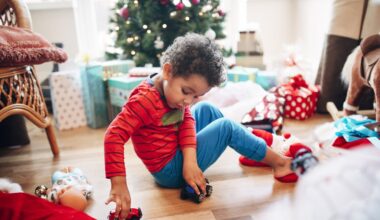 A little boy plays with some toy cars he has received as a Christmas present in front of the Christmas tree.