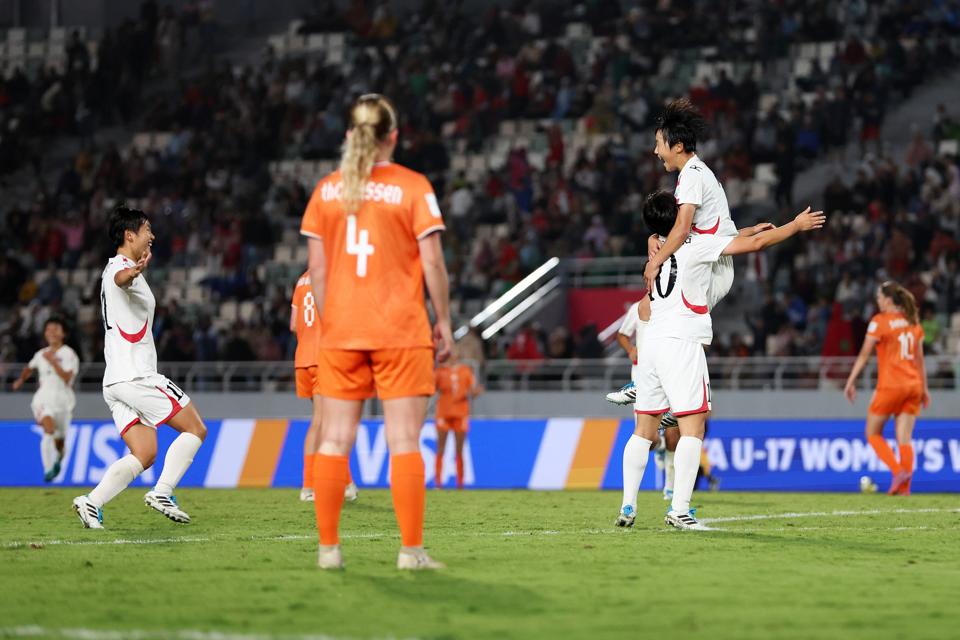 North Korean players celebrating after scoring in the 2025 U-17 Women's World Cup final, with Dutch players looking on.