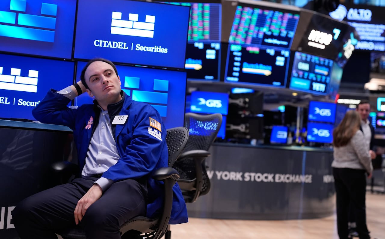 A man sits amid the monitors and desks of a stock exchange, looking off camera. 