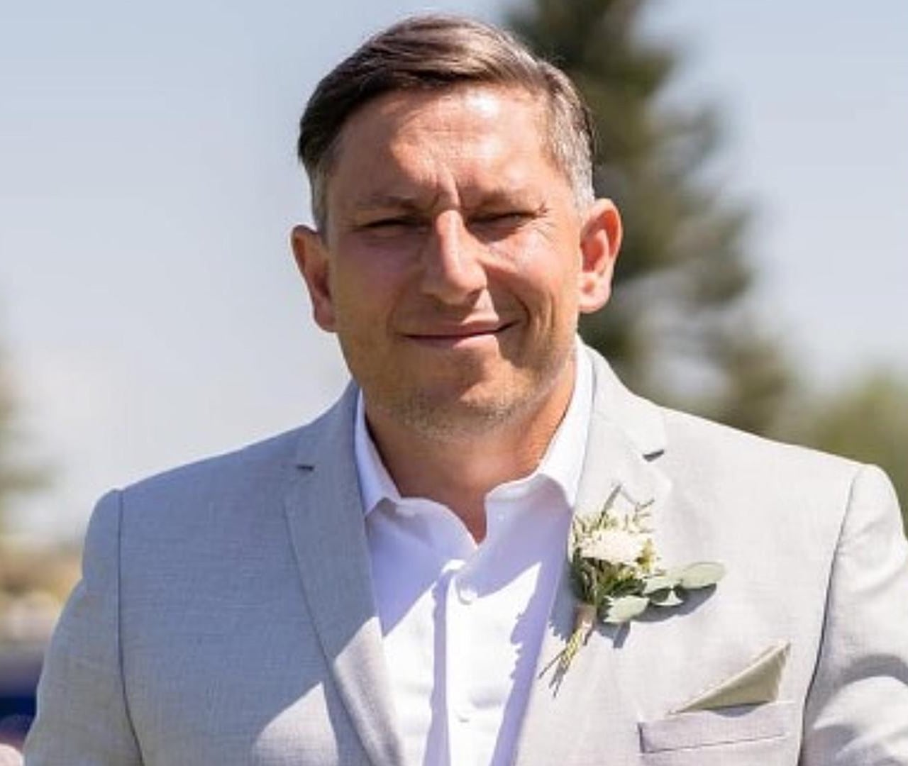 A man in a light-coloured suit squints in the sun.