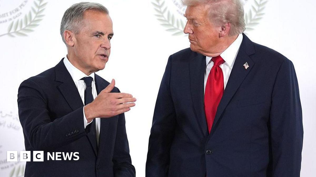 President Donald Trump greets Canada's Prime Minister Mark Carney during a world leaders' summit on ending the Gaza war on October 13, 2025 in Sharm El-Sheikh, Egypt. Prime Minister Mark Carney is on the left, wearing a black tie and a black suit. President Trump is on the right, wearing a dark blue suit and a red tie. PM Carney is gesturing as he speaks to Trump, who appears to be listening. Behind them is a white backdrop.