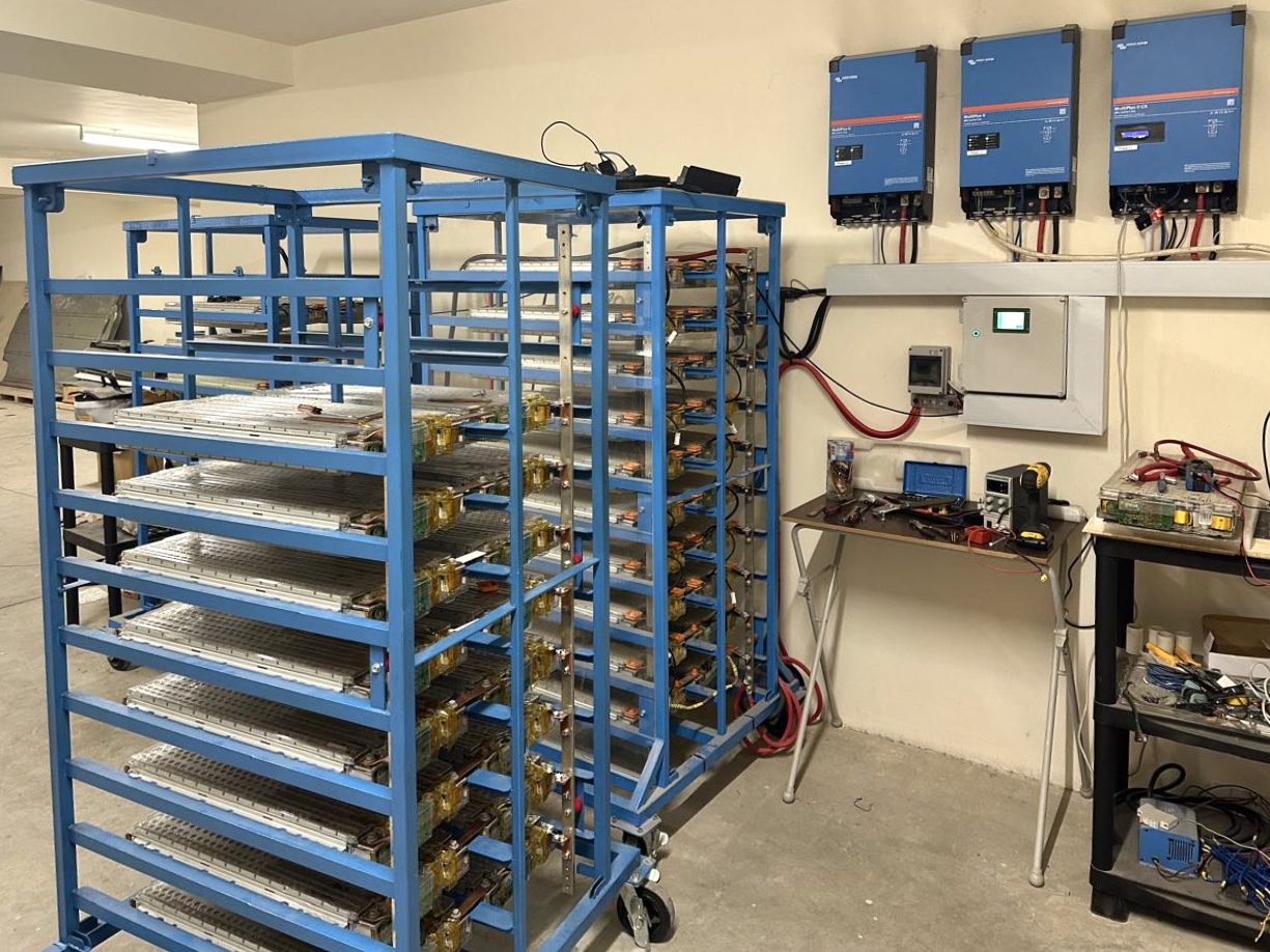 Reconditioned Tesla batteries lying flat on two large blue trolleys form part of a homemade energy storage system
