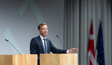 Mann in Anzug an Rednerpult, hinter ihm Flaggen.