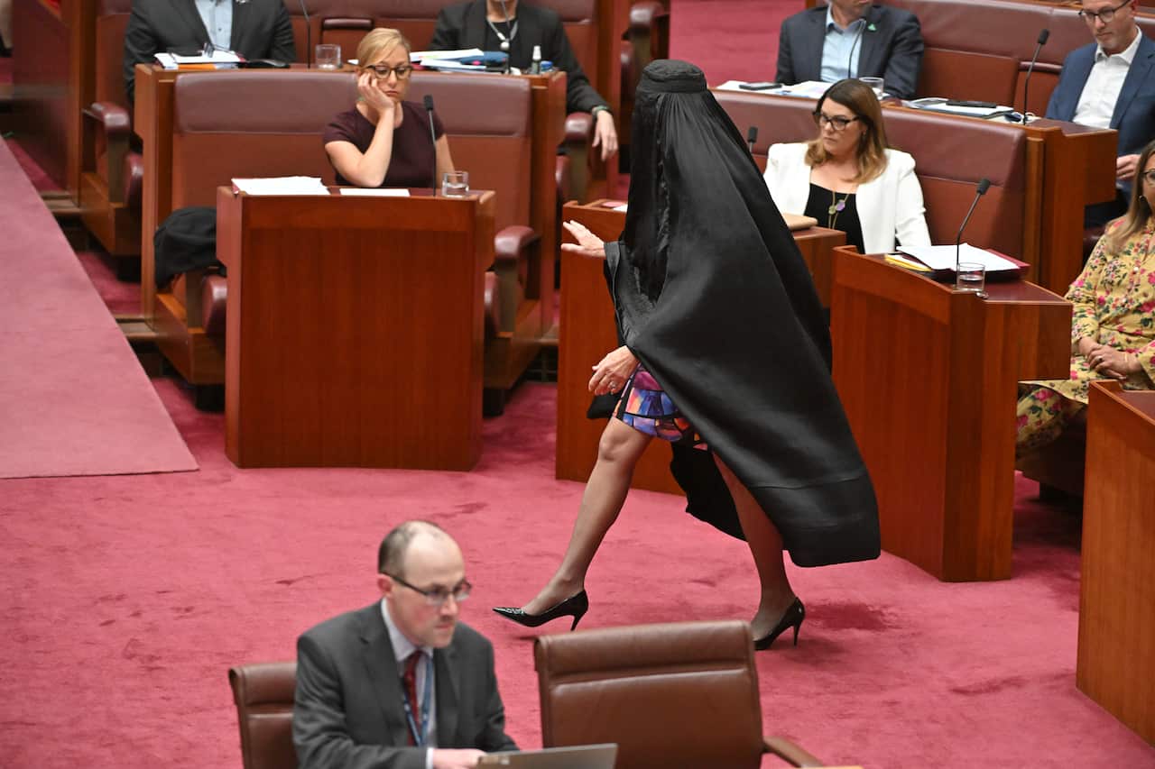 A woman wearing a black burqa walking on red carpet in Senate chamber