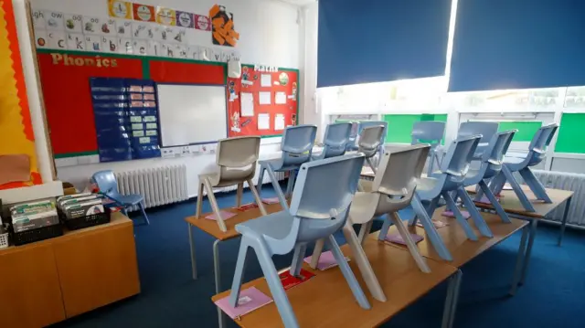 An empty classroom with chairs on tables and blinds half closed